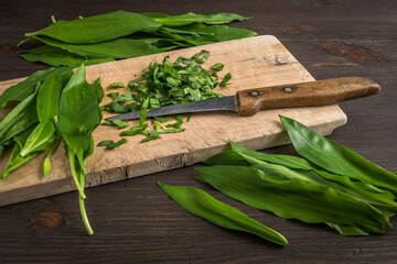 Chopped leaves of wild garlic on a wooden desk with a knife
