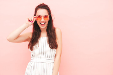 Portrait of young beautiful smiling female in trendy summer hipster overalls clothes. Sexy carefree woman posing near pink wall in studio. Positive model having fun indoors. Cheerful and happy