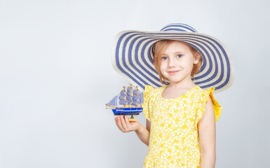 Obraz premium A girl in a wide-brimmed hat holds a toy boat in her hands.