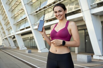 Beautiful young sportswoman holding smartphone and looking at camera