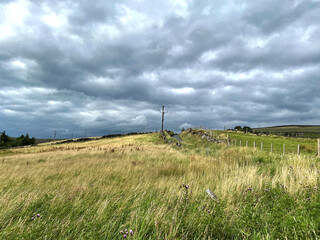 Fototapeta premium Rain clouds passing over the brow of, Gall Lane, with fields, wild grass, and dry stone walls above, Todmorden, Yorkshire, UK