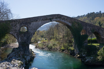 Fototapeta na wymiar Roman bridge of Cangas de Onis, Asturias, over the Sella river, with no people. Victory cross hanging from the bridge..
