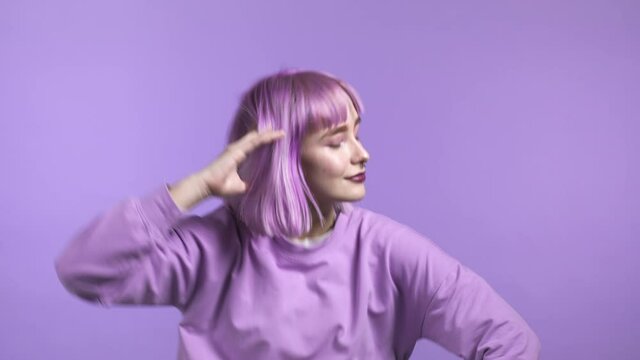 Attractive woman with purple hairstyle dancing on violet studio background. Girl zoomer in positive mood.