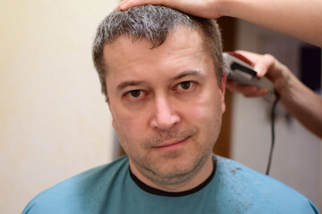 Obraz premium A man is trimmed with a hair clipper and sits facing the camera. Perhaps at home in a lockdown