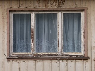 Fenster mit Gardinen in alter Hausfassade aus Holz mit blätternder Farbe 