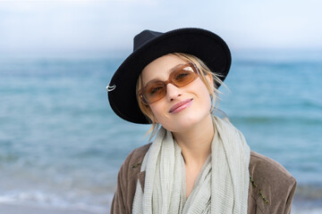 Portrait of a stunning young girl in glasses and hat on the beach with a slight smile 