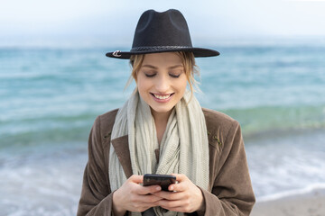 Stunning young woman holding a mobile phone with a smile while texting a massage 