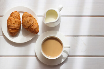 Cozy morning flat lay. Cup of coffee with milk and two croissants on a plate on white wooden table. Morning concept. Top view