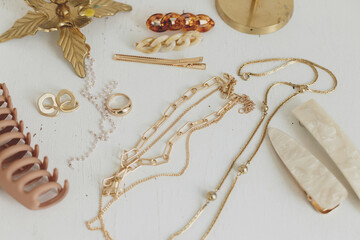 Modern golden jewellery, hair clips on white wood table with vintage candlesticks. Boho accessories