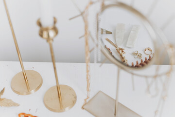Modern golden accessory and hair clips reflected in boho mirror on white table with vintage candles