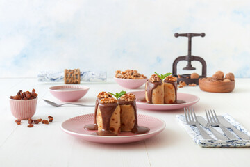 Pancakes stuffed with raisins and crushed walnuts, with chocolate cream topping. White wooden table, no people.