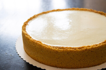 Close up of a New York cheesecake on a black table with a light reflection from the corner.