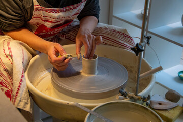 hands of a potter making a small clay pot while the wheel is spinning