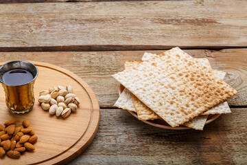 Obraz na płótnie Canvas Matzah on a napkin and a round board with nuts and a glass of wine for kiddush on a wooden table.