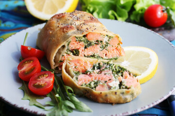 Strudel with salmon, spinach, cheese, arugula, lemon and tomatoes on blue background