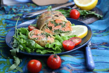 Strudel with salmon, spinach, cheese, arugula, lemon and tomatoes on blue background