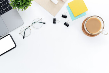 Top view of a desk with a laptop, eyeglasses, notebooks, post-it, and mobile phones isolated on  white background with copy space