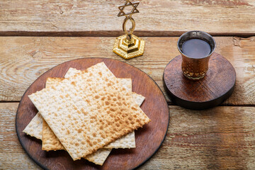 On a round wooden brown board, matzah and a glass of kiddush wine are next to the menorah on the table.