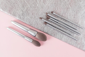 Set of silver color professional makeup brushes in isometric line on pink and gray colored composed background. Creative concept of beauty. Copy space. Flat lay.