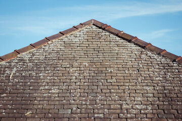 A triangle or hip roof end showing the ridge, mortar and lichen on the old damaged traditional stone slate tiles