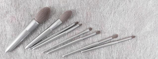 Set of silver color professional makeup brushes on gray colored background. Creative concept of beauty. Banner. Copy space. Flat lay.
