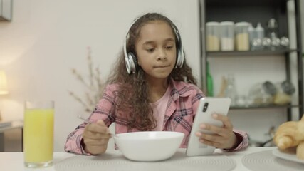Teen girl having meal in earphones scrolling smartphone, unhealthy eating habits