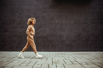 Side view of trap girl in tracksuit walking with hands in her pockets and listening music.