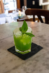 green mint cocktail with ice on a marble table in a bar.