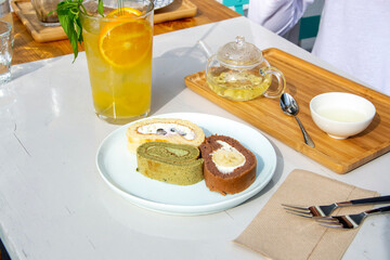 matcha, vanilla and chocolate banana swiss roll cake slices with green tea and orange lemonade in a cafe