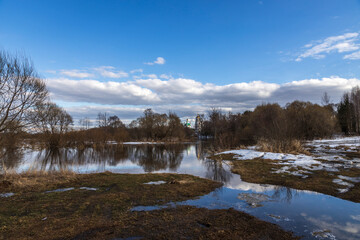 River flood on a spring day. Dry grass is visible from under the snow. The land is flooded with water.