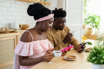 african man and woman sitting at the table in the kitchen with mobile phones 