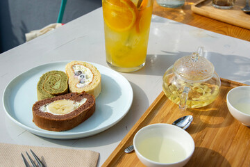matcha, vanilla and chocolate banana swiss roll cake slices with green tea and orange lemonade in a cafe