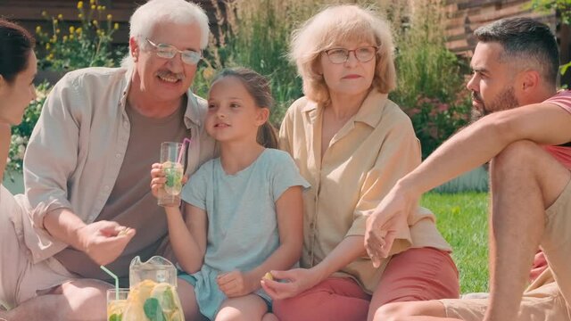 Medium PAN shot of big multigenerational family of five having good time together spending summer day in backyard chatting and drinking fresh lemonade