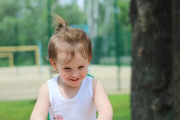 Little smiling child is riding a swing in the park. Blurred playground in the background