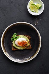 Rye bread avocado hummus toast with poached egg on black plate