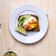 Poached egg on smashed avocado on brown toast served on white plate