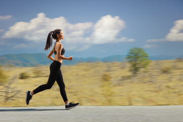 Fototapeta premium Young woman jogging on a road in a countryside on an open road