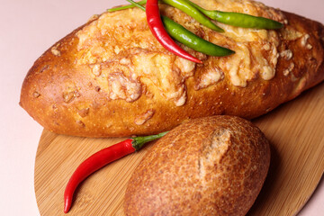 Fresh bread on a cutting board with red and green chili peppers.