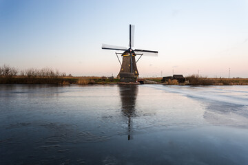 Windmills at Kinderdijk, close to Rotterdam in The Netherlands, in winter with ice on canal at sunset.