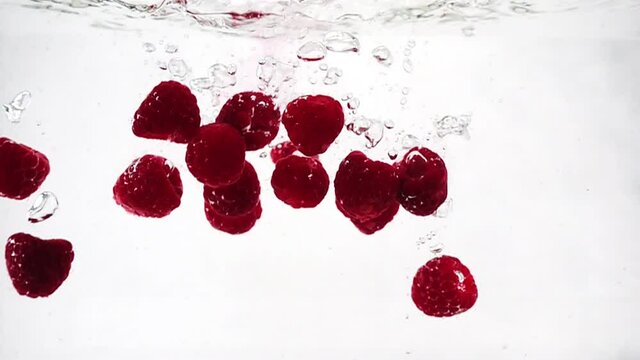 A beautiful ripe raspberry is immersed in a container of water with bubbles in slow motion. A raspberry isolated on a white background. Theme of vegetarian and raw food as a lifestyle. Cocktail.