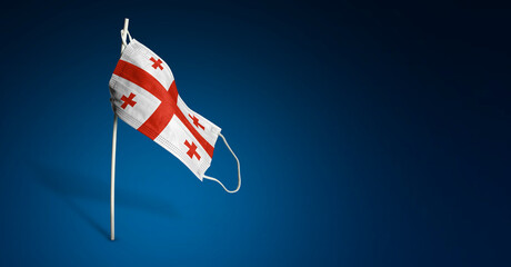 Georgia mask on dark blue background. Waving flag of Georgia painted on medical mask on pole. Concept of The banner of the fight against the epidemic coronavirus COVID-19. Copy space