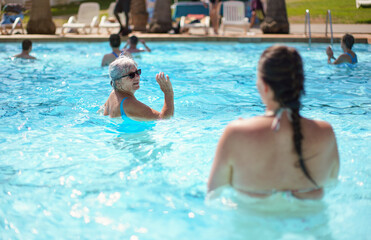 Elderly senior woman with grey hair, wearing blue swimsuit doing water aerobics in hotel pool