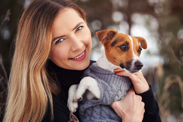 Young woman holding her Jack Russell terrier dog wearing warm winter clothing on hands