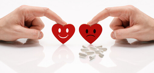 Two hearts with happy and sad emotion. There are pills next to the sad emotion. The concept of comparing a healthy heart and a sick one.