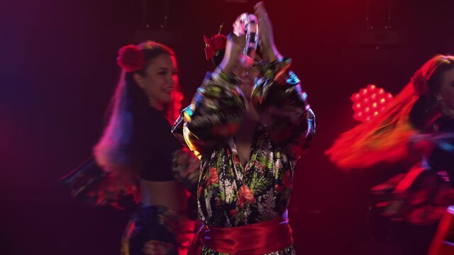 Three adorable woman and one man are dancing in gypsy costumes. Theatrical performance of folk romany dances. Black background and red studio spotlights. Close up.