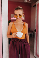 Charming adorable lady with blond hair wearing orange t-shirt drinking coffee outside in summer warm day