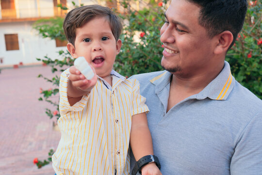 Latino Father Holding His Son While Eating Candy