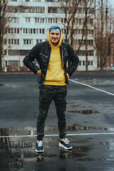 Young man standing on sports stadium on background of high-rise building. Handsome guy with blue hair posing on city street in springtime.