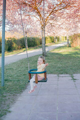 A little cute girl is riding a swing in a blooming garden. Spring.