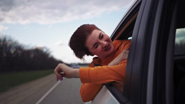 Happy Beautiful Girl Riding in the Back Seat of a Car Looks Out the Open Window and Smiles. Traveling Woman Enjoys the Stunning Scenery. Slow Motion.